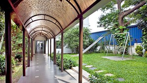 A covered walkway with a curved roof, surrounded by greenery and a grassy area with a swing set. - BRAC-CDM Savar (Savar)