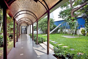 Uma galeria coberta com telhado curvo, cercada por vegetação e uma área gramada com balanço.