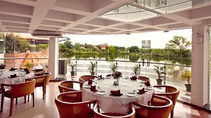 A restaurant with round tables set for dining, overlooking a body of water. - BRAC-CDM Savar (Savar)
