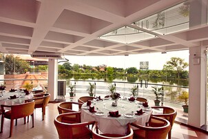 Restaurante com mesas redondas preparadas para refeições, com vista para um corpo de água.