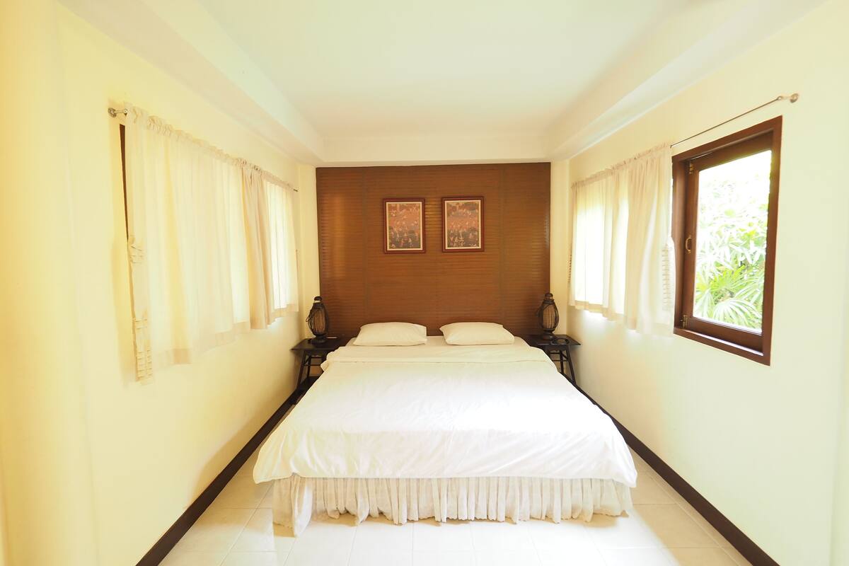 Un dormitorio con una cama grande, dos mesitas de noche, un cabecero de madera y dos cuadros enmarcados en la pared.