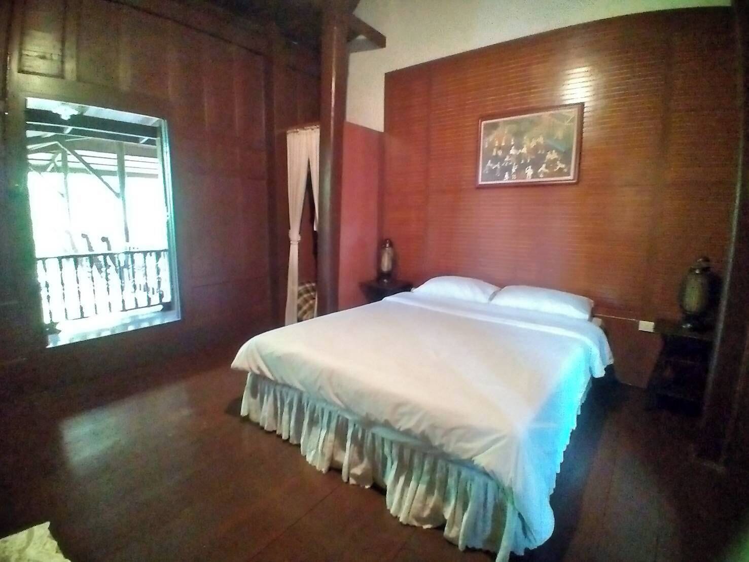 A bedroom with a large bed, wooden walls, a window with a view, and a painting on the wall.