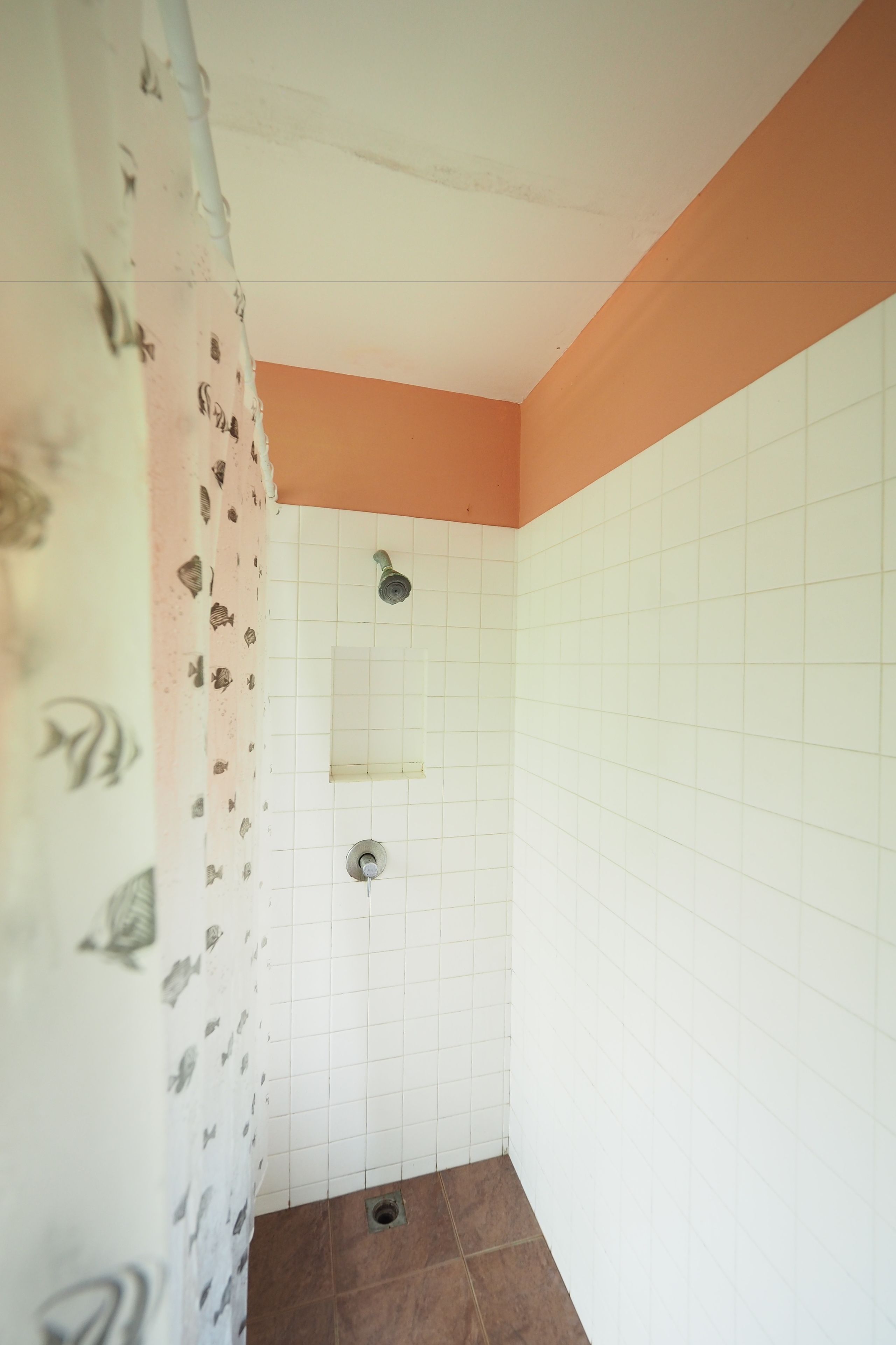 A small bathroom with white tiled walls, a shower with a single faucet, and a drain.