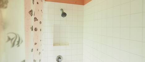 A small bathroom with white tiled walls, a shower with a single faucet, and a drain.