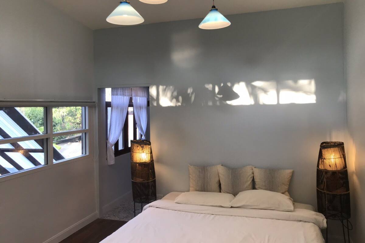 Un dormitorio con cama, dos lámparas de noche, una ventana con cortinas y vistas al exterior.