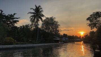 A calm river with a sunset in the background, surrounded by trees and a few buildings.