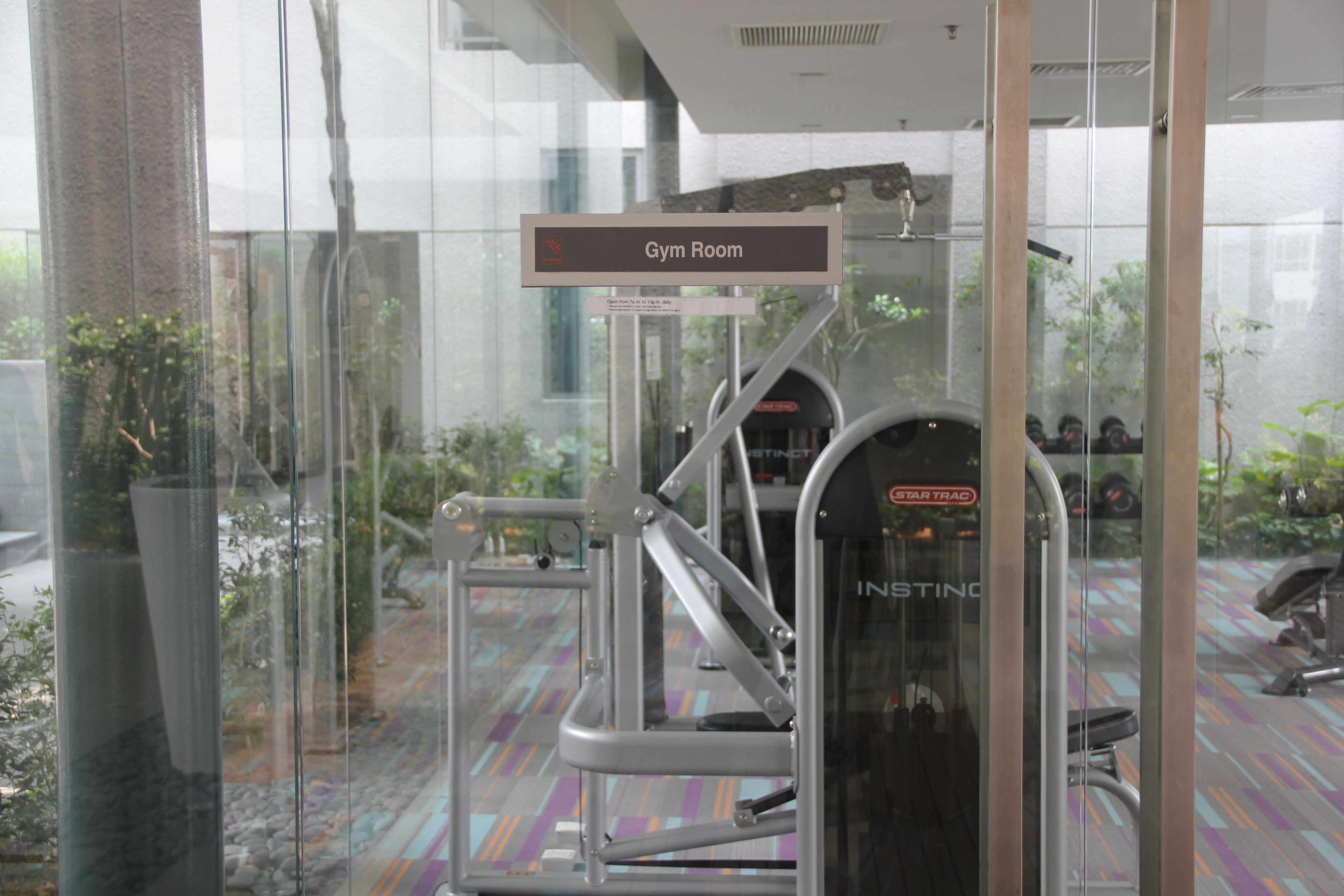 A gym room with exercise equipment, a sign indicating the room, and a view through glass walls.