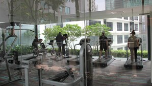 Ein Fitnessstudio mit Laufbändern und Trainingsgeräten, großen Fenstern und Blick auf Gebäude.