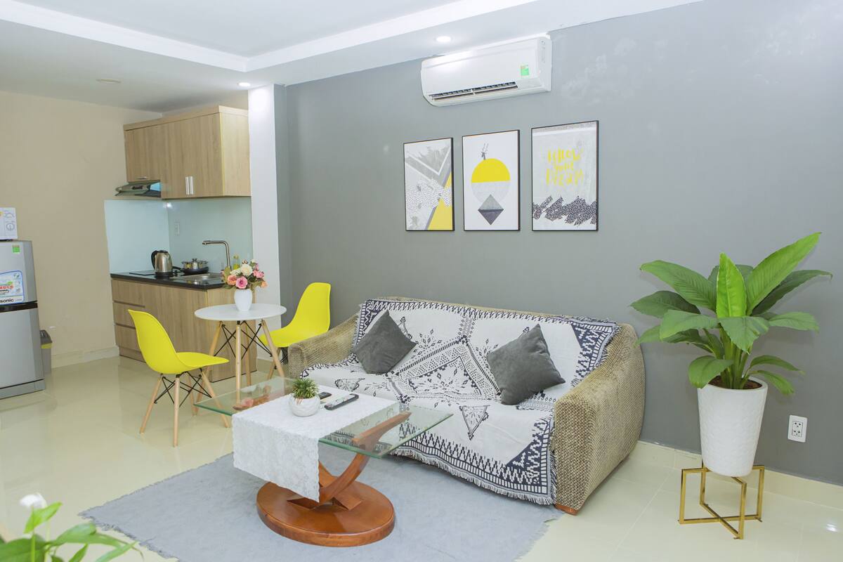 A compact living space with a kitchenette, a sofa, a dining table with chairs, and a potted plant.