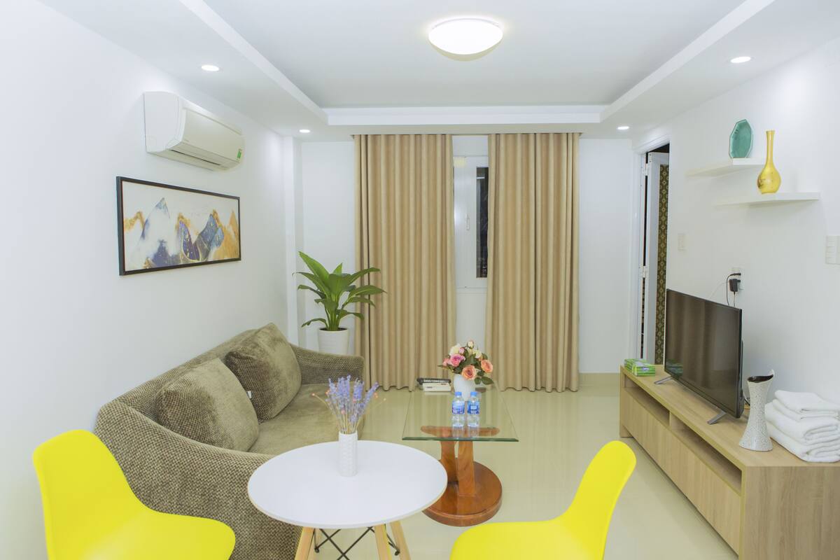 A modern living room with a sofa, two yellow chairs, a glass coffee table, a TV, and a plant.