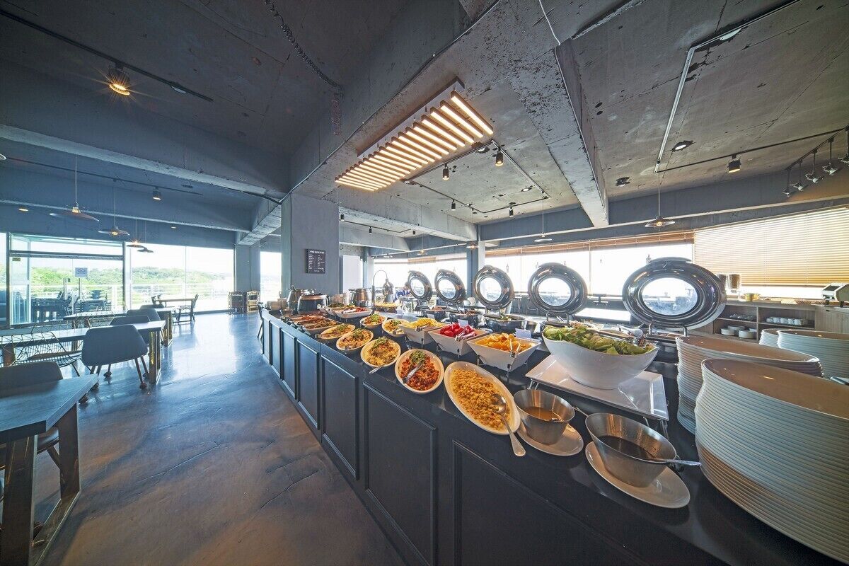 A buffet setup with various dishes, a long counter, and seating area with tables and chairs.
