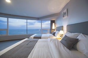 A hotel room with two beds, a large window with a view of the sea, and a lamp on the nightstand.
