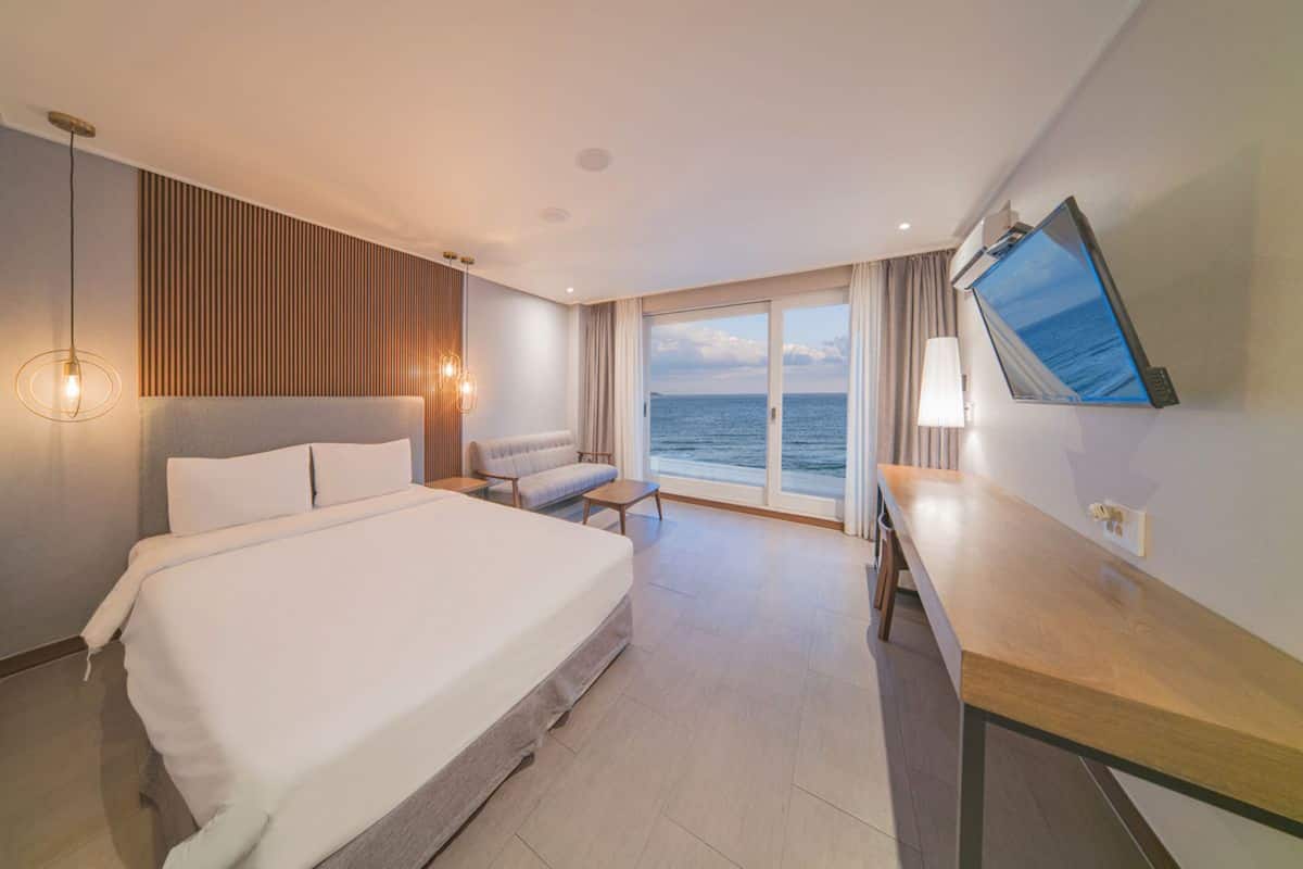 Une chambre d’hôtel avec un grand lit, un bureau, une chaise et une vue sur la mer.