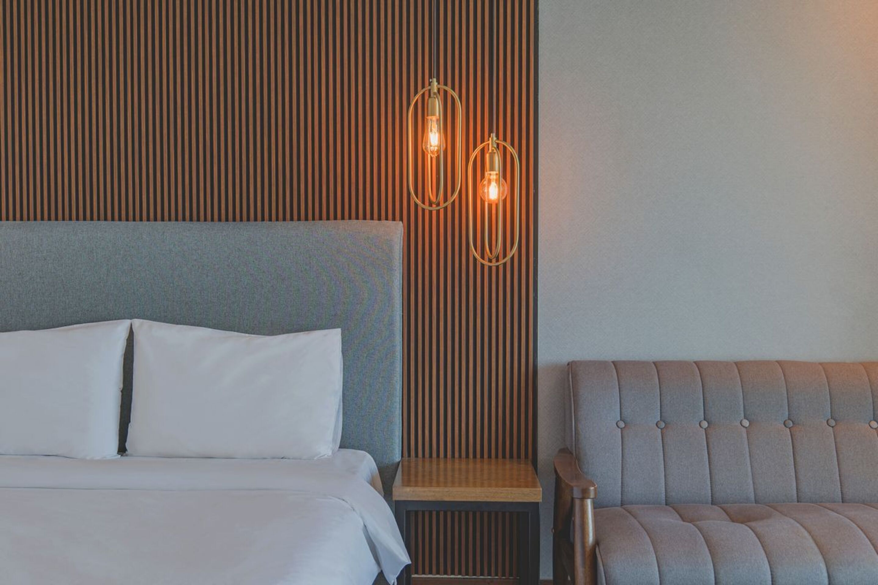 A hotel room with a bed, a chair, and a wall-mounted light fixture.