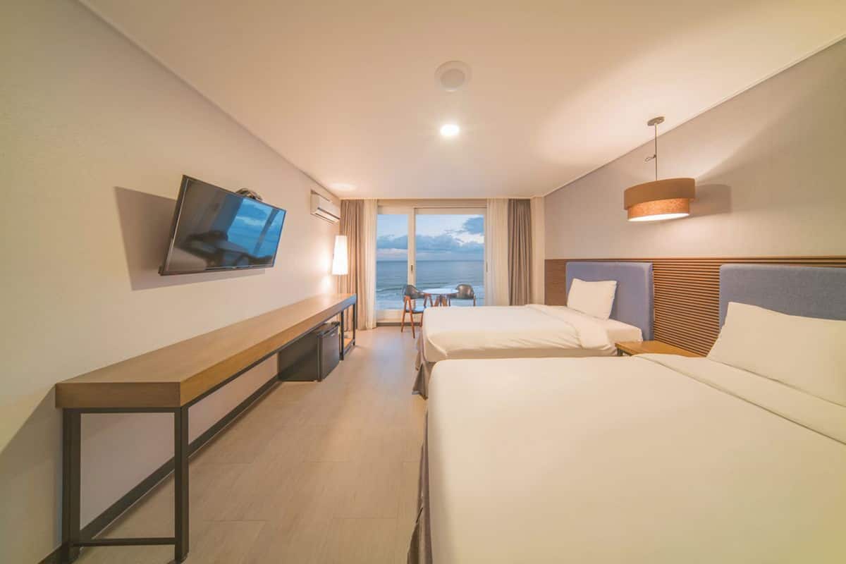 Une chambre d’hôtel avec deux lits, une télévision, un bureau et une vue sur la mer.