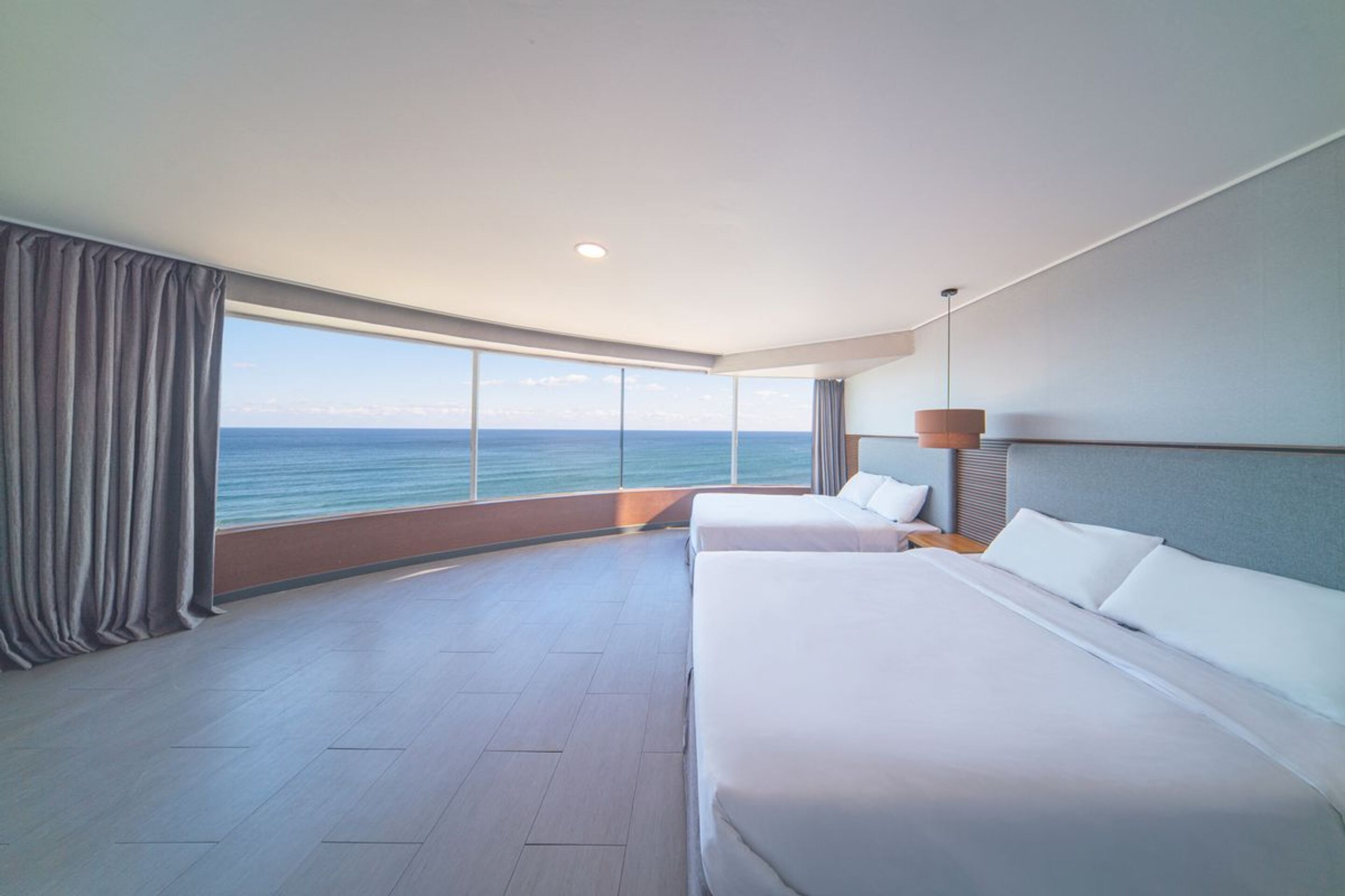 Ein modernes Hotelzimmer mit zwei Betten, einem großen Fenster mit Meerblick und einem minimalistischen Design.