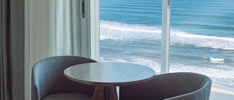 A room with a view of the ocean, a round table, and two chairs.