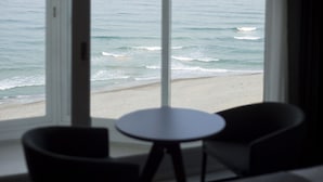 A room with a view of the ocean through large windows, a round table, and two chairs.