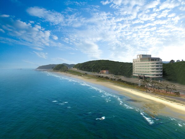 Un hotel costero de diseño moderno, ubicado junto a la playa con vista al océano y colinas al fondo.