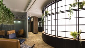 A reception area with a curved black counter, wooden flooring, and seating with blue and brown upholstery. - The Capsule Hotel - Hostel (Haymarket)