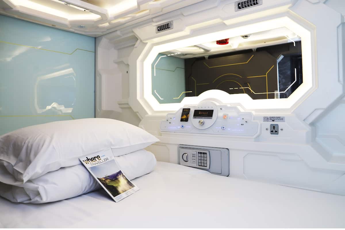 A modern hotel room with a large window, a control panel, and a magazine on the bed.