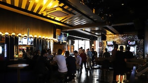 A bar area with multiple stools and tables, a counter with a menu, and a few people seated and standing. - The Capsule Hotel - Hostel (Haymarket)