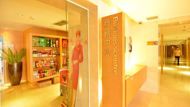 A hotel reception area with a wooden reception desk, a glass display case with various items, and a large potted plant. - Qingdao Wushengguan Holiday Hotel (Qingdao)
