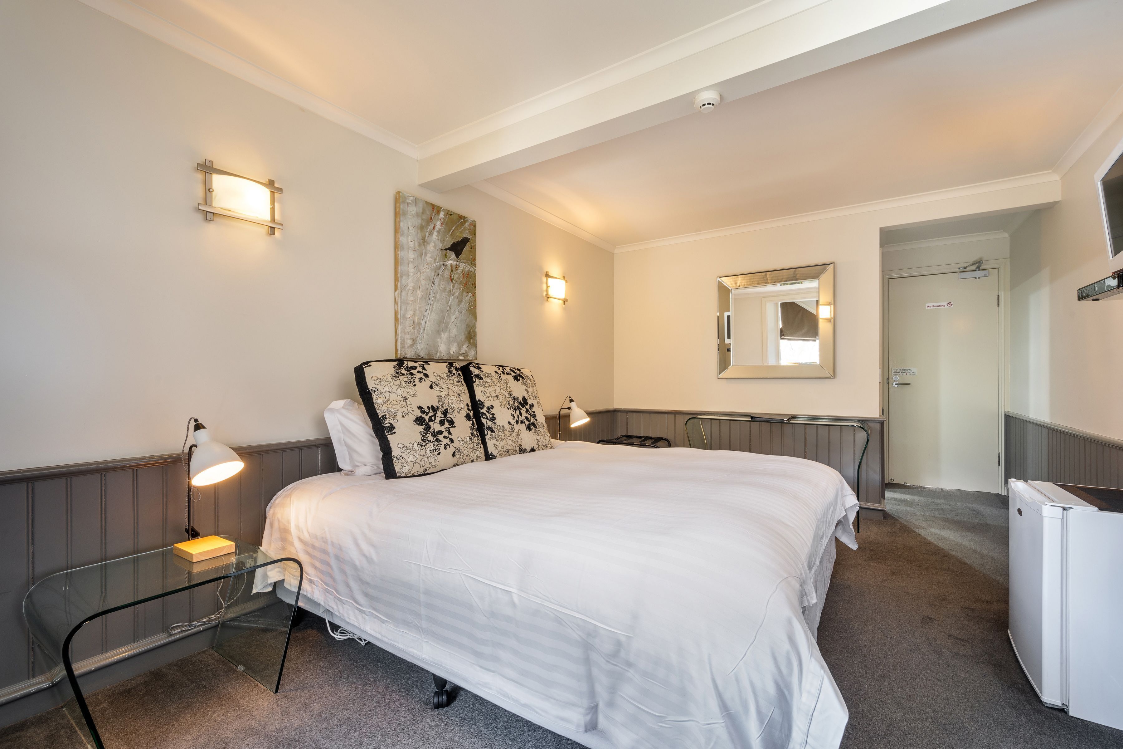 A neatly arranged hotel room with a bed, bedside table, lamp, and a mirror on the wall.