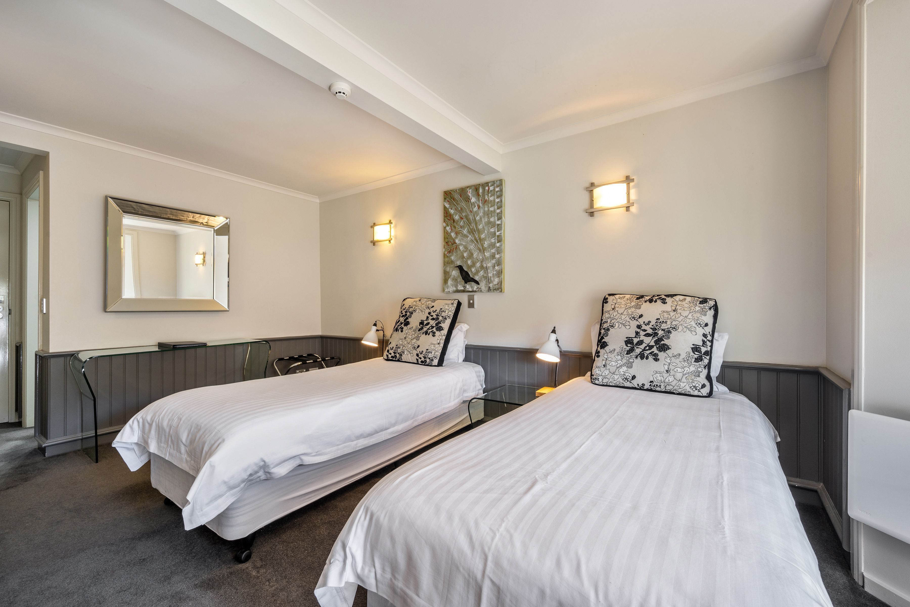 Ein Hotelzimmer mit zwei Einzelbetten, einem großen Spiegel, Wandleuchten und einem dekorativen Gemälde.