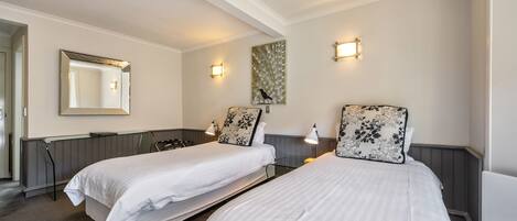 A hotel room with two single beds, a large mirror, wall-mounted lights, and a decorative painting.
