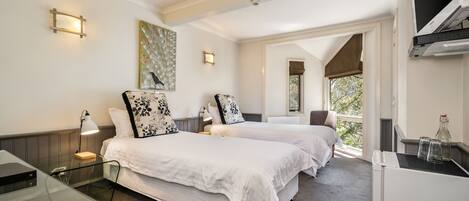 A hotel room with two beds, a desk, a chair, a TV, and a window with a view of greenery.