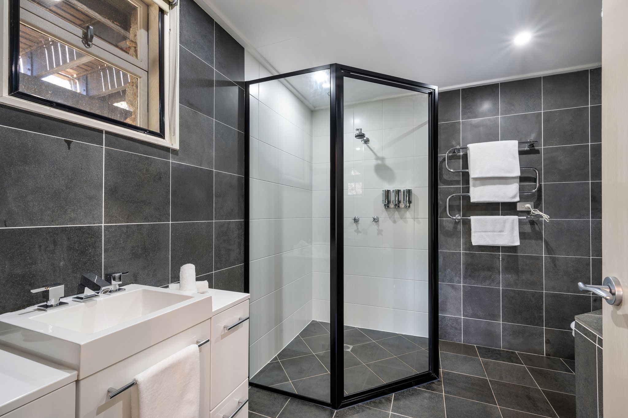 A modern bathroom with a glass-enclosed shower, a large sink, and dark tiled walls.