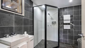 A modern bathroom with a glass-enclosed shower, a large sink, and dark tiled walls.