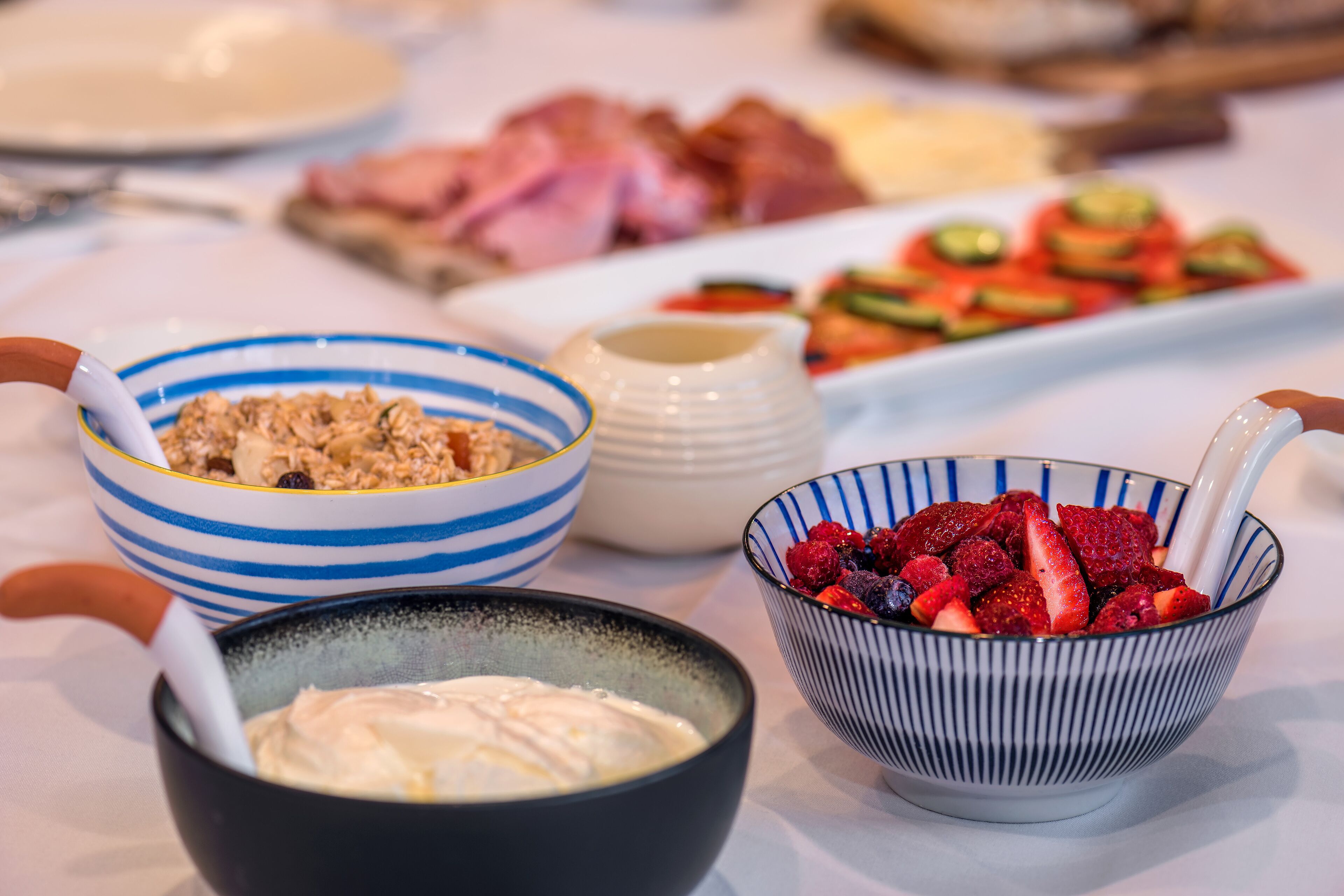 Una mesa con diferentes alimentos, como tazones de yogur, granola y frutos rojos frescos.