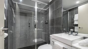 A modern bathroom with a glass-enclosed shower, a white toilet, and a large mirror above the sink.