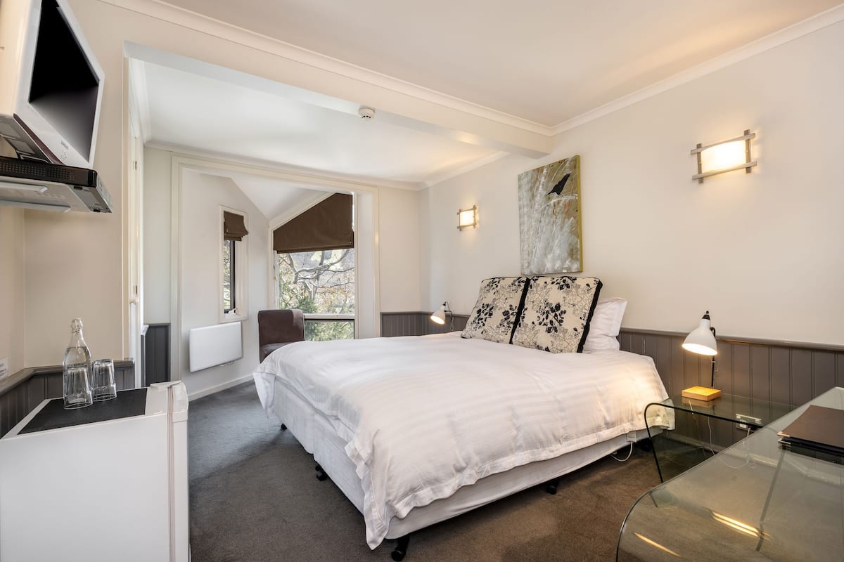 A bedroom with a large bed, a glass table, a lamp, and a painting on the wall.
