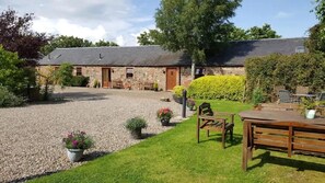 A stone building with a gravel driveway, a grassy lawn, and outdoor seating.