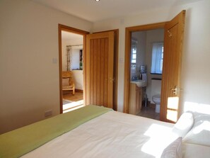 A bedroom with a bed, a wooden wardrobe, and a bathroom visible through an open door.