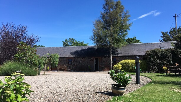 A stone building with a gravel driveway, surrounded by greenery and a clear blue sky. - The Courtyard (Perth)