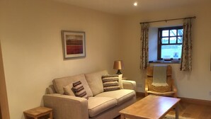 A living room with a sofa, a coffee table, a lamp, a chair, a rug, a picture on the wall, and a window with curtains. - The Courtyard (Perth)