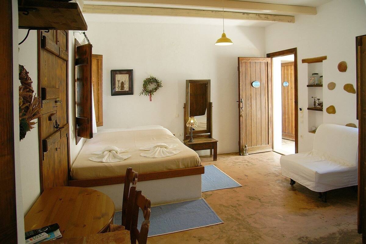 Una habitación con una cama, una silla, una mesa, una lámpara, un espejo y una puerta.