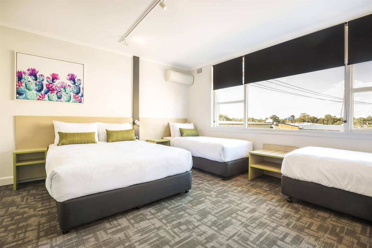 A hotel room with two beds, a large window, and a cactus artwork on the wall.