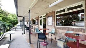 An outdoor cafe with tables and chairs, a brick wall, and a window overlooking the street. - Nightcap at Hume Hotel (Yagoona)