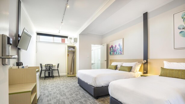 A hotel room with two beds, a desk, a chair, a TV, and a painting on the wall. - Nightcap at Hume Hotel (Yagoona)