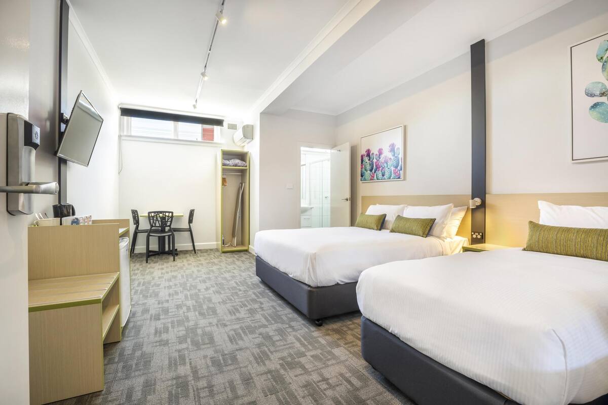 A hotel room with two beds, a desk, a chair, a TV, and a painting on the wall.