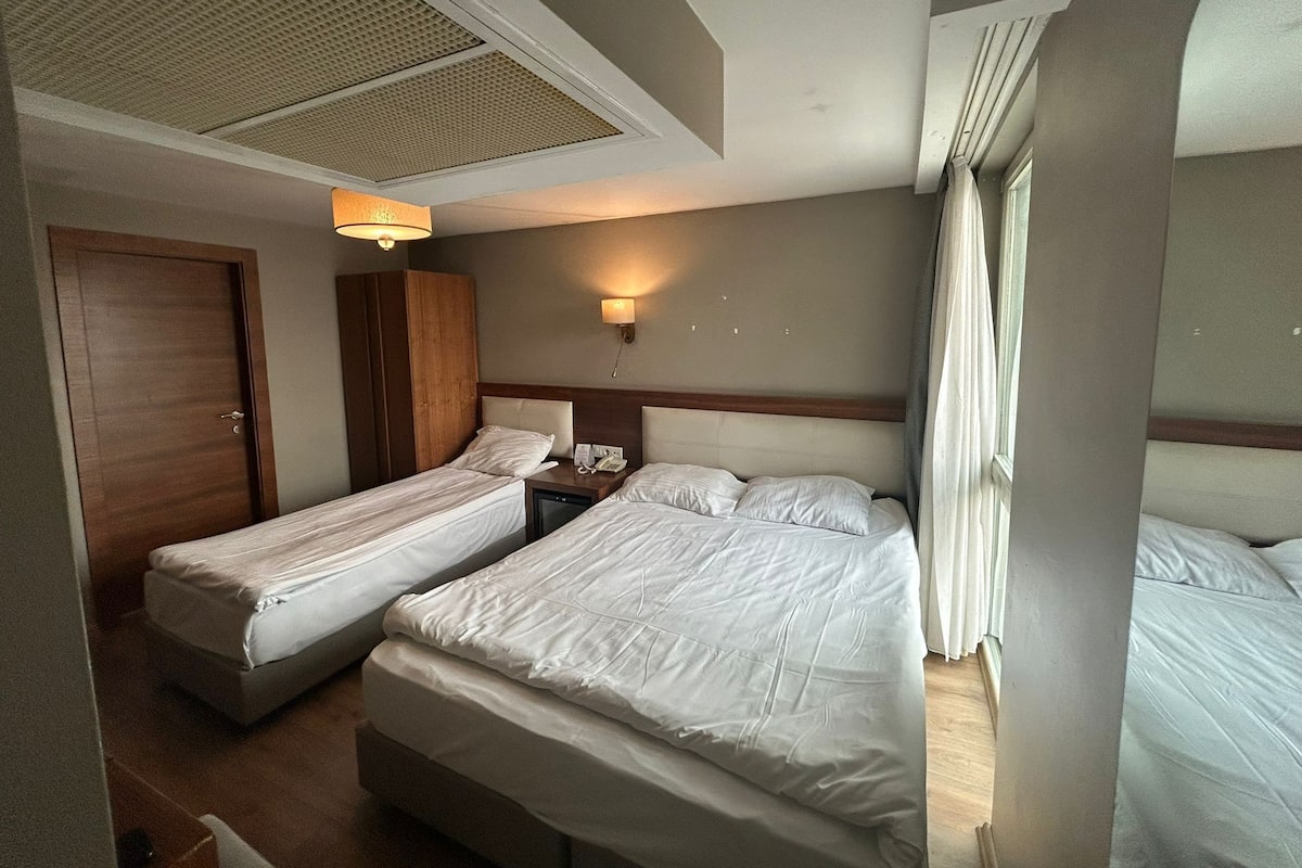 Ein Hotelzimmer mit zwei Einzelbetten, einem Holzschrank, einem kleinen Nachttisch mit Lampe und einem Deckenlüfter.