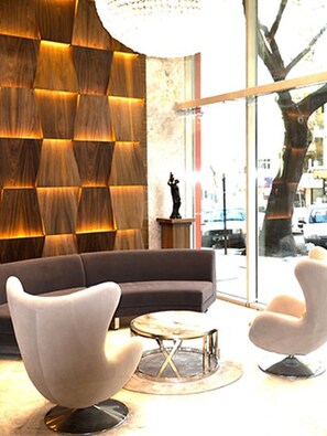 Un salón moderno con un papel tapiz estampado, un sofá, dos sillones y una mesa de centro redonda.
