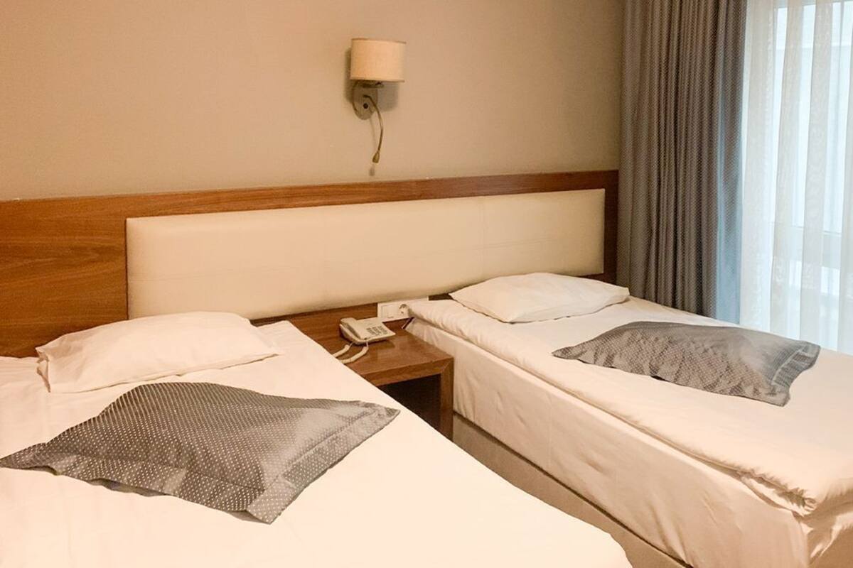 Ein Hotelzimmer mit zwei Einzelbetten, einem Holzkopfteil, einem Nachttisch mit Lampe und einem Vorhangfenster.