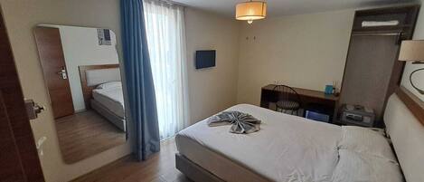 A hotel room with a bed, a desk, a chair, a TV, and a wardrobe.