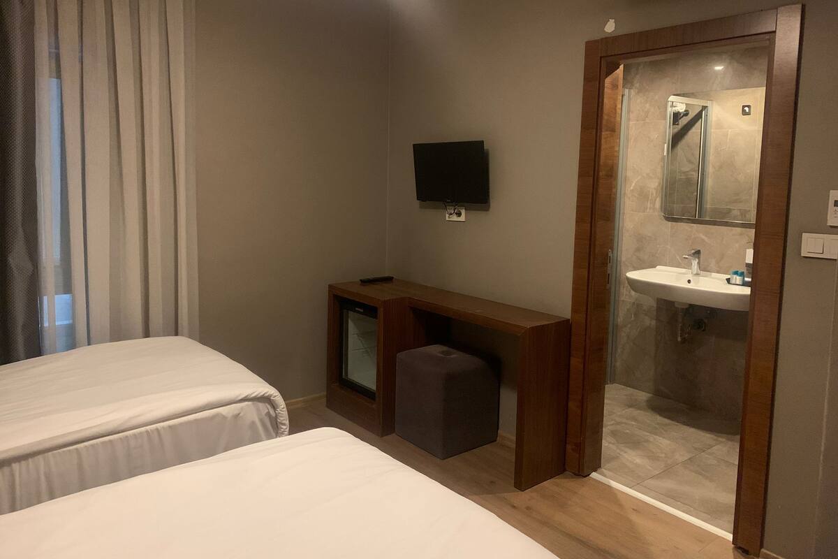 Ein Hotelzimmer mit zwei Betten, einem Fernseher, einem kleinen Schreibtisch und einer Duschkabine.